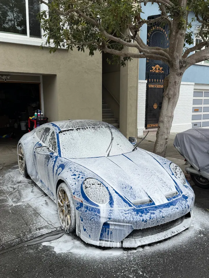 Blue and white Porsche 911 covered in foam during a maintenance wash